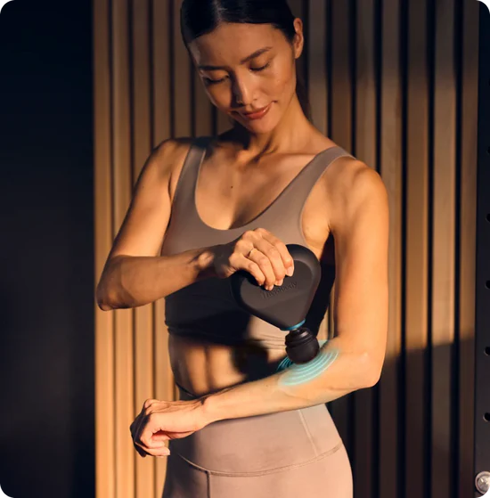 Woman using the Theragun mini plus with cold attachment in a gym