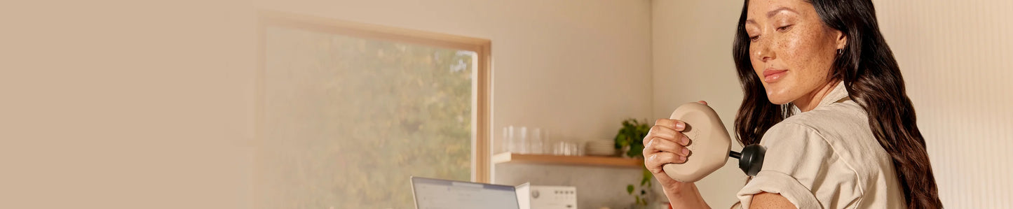 Massagepistol från Therabody - kvinna använder en liten Theragun Mini portabel massagepistol på sin överarm. Beige färger och bakgrund